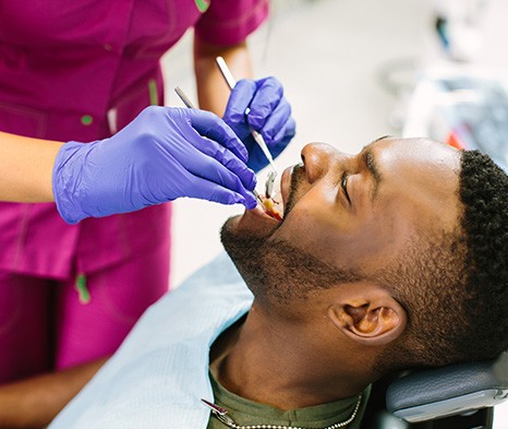 Man undergoing dental examination by dentist in magenta scrubs