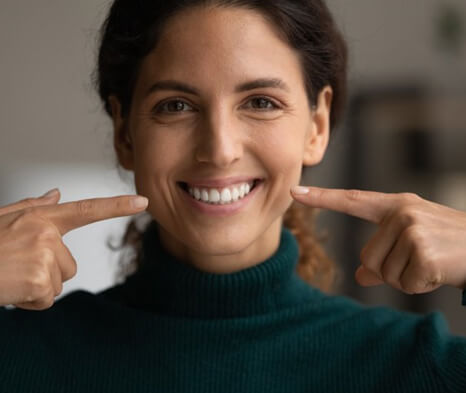 a woman smiling and pointing at her teeth