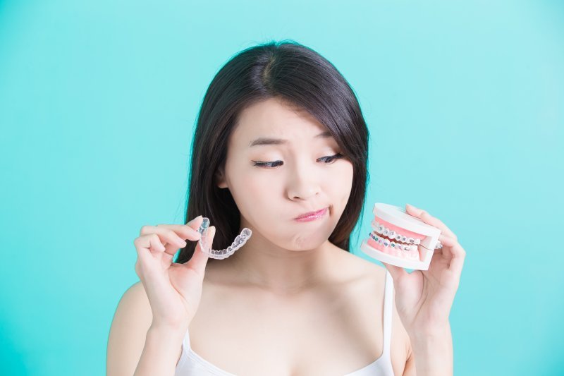 A woman holding an aligner in one hand and mock braces in the other